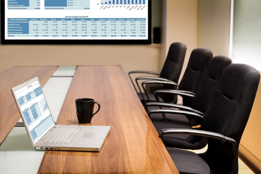 A conference room with four empty chairs and an open laptop on the table next to a coffee mug.