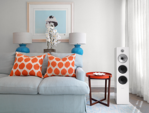 A blue couch with orange pillows, with other blue and orange home decor, next to a white, floor-standing Bowers and Wilkins speaker.