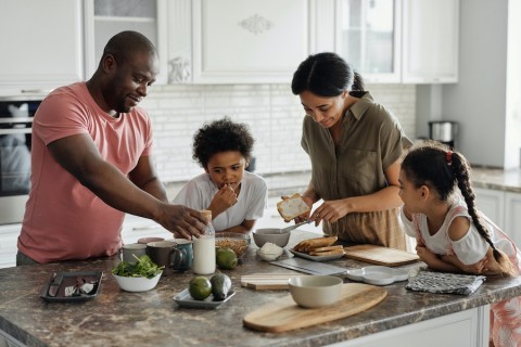 Family of four gathered around the kitchen counter having breakfast.  