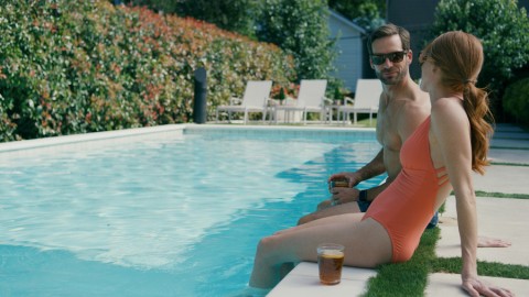 A man and woman sitting by the pool with an outdoor entertainment speaker in the background. 
