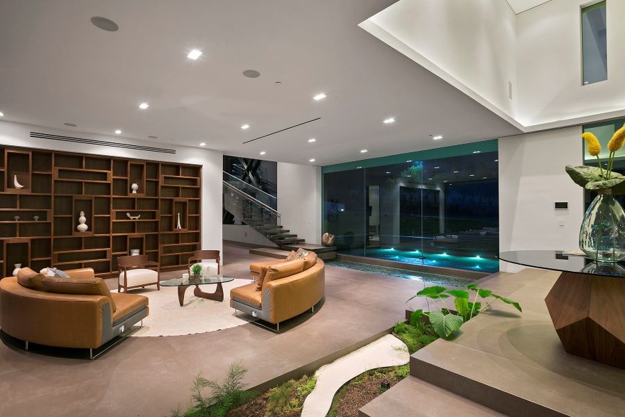 A modern home with recessed lighting, in-ceiling speakers, and blue-lit pool outside the windows.