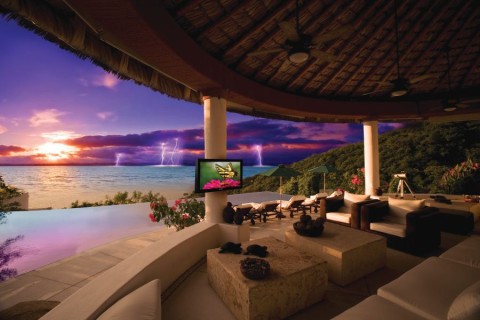 An outdoor Seura TV on a large patio on the ocean with a storm in the distance.